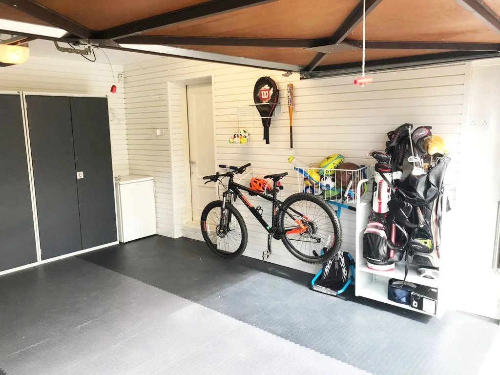 A garage conversion with a bike rack, shelves holding golf bags and a wall-mounted basket with sports equipment in it.